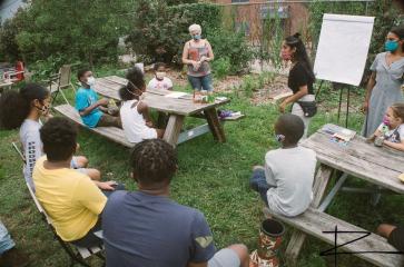 The students are in the garden learning about edible herbs from lead teacher