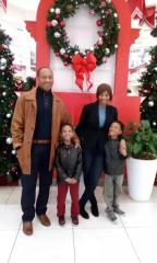 A man, his wife, and their two young boys stand in front of a Christmas-themed display, smiling. 