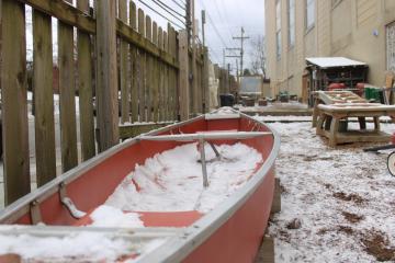 Snow lightly covers a wooden water table and a red canoe, perfect for pretending