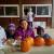 Three african american children sitting behind some pumpkins