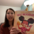 Screenshot of a virtual presentation showing the speaker, Sarah, an Asian-American female. She is holding a book in her hands, showing her children’s book illustration skills to the classroom. 